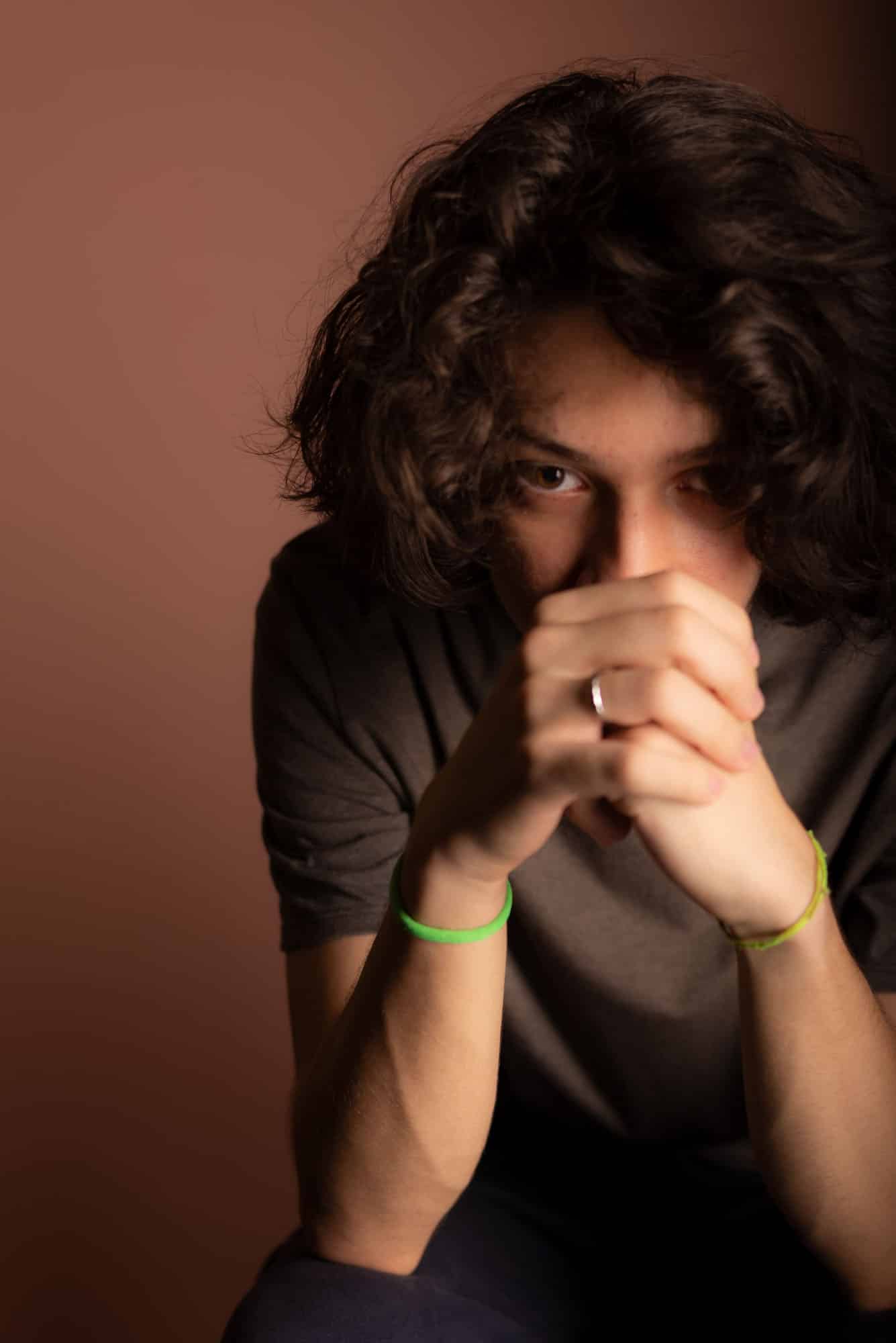 Caucasian male with curly hair sitting in front of a wall in a thoughtful pose